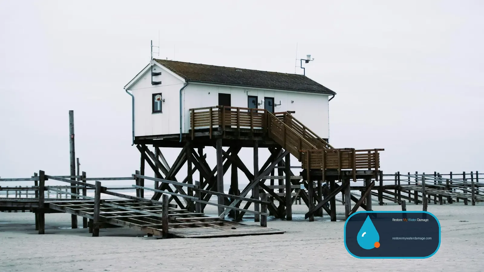 White house raised on stilts above the shore, an elevated design linked to water damage restoration Staten Island, NY